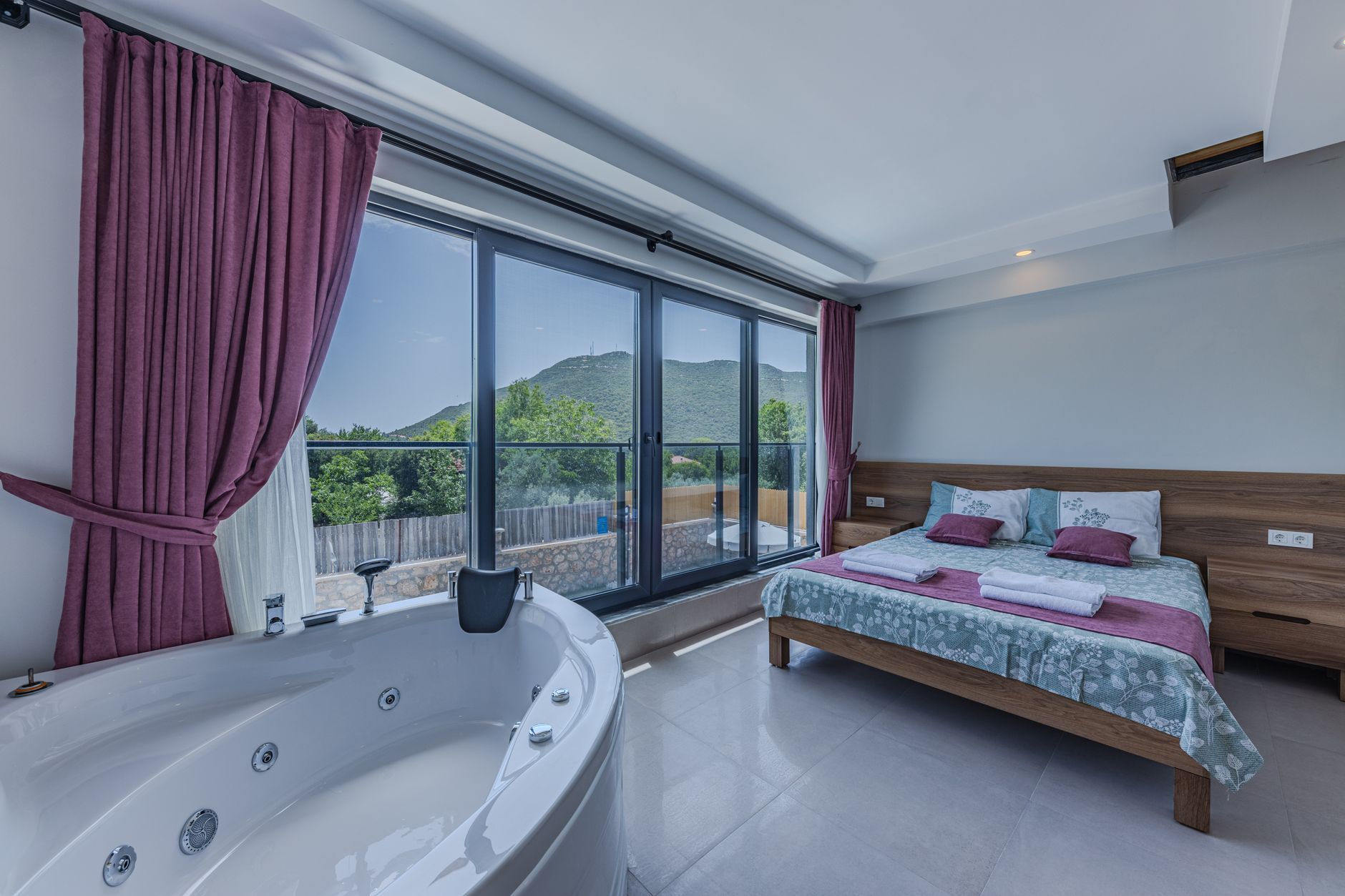 Spacious recovery suite featuring a jacuzzi, bed, and garden view windows in a thermal wellness resort.