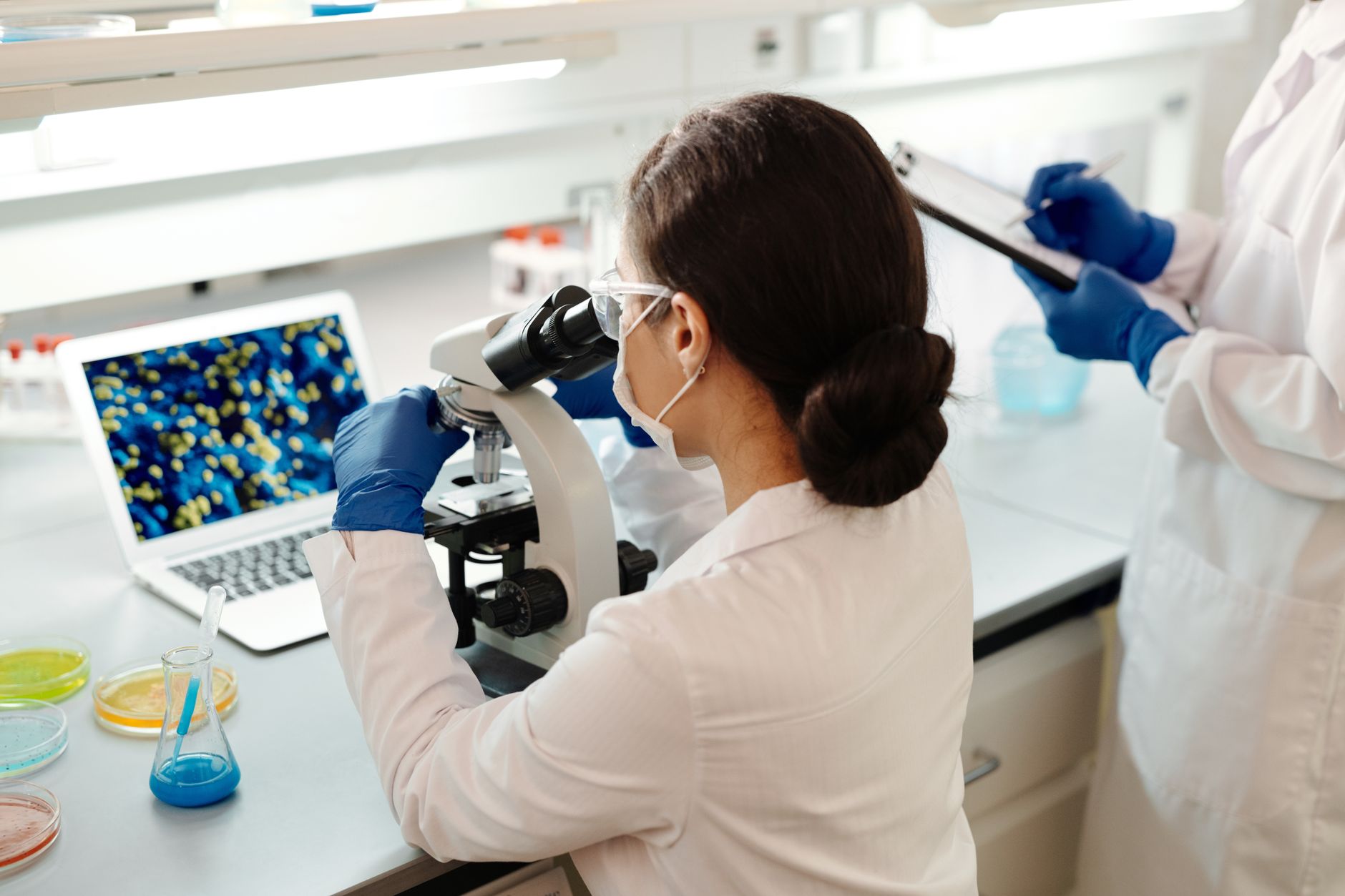 A pathologist uses a microscope to examine thyroid cytology slides with a laptop display.