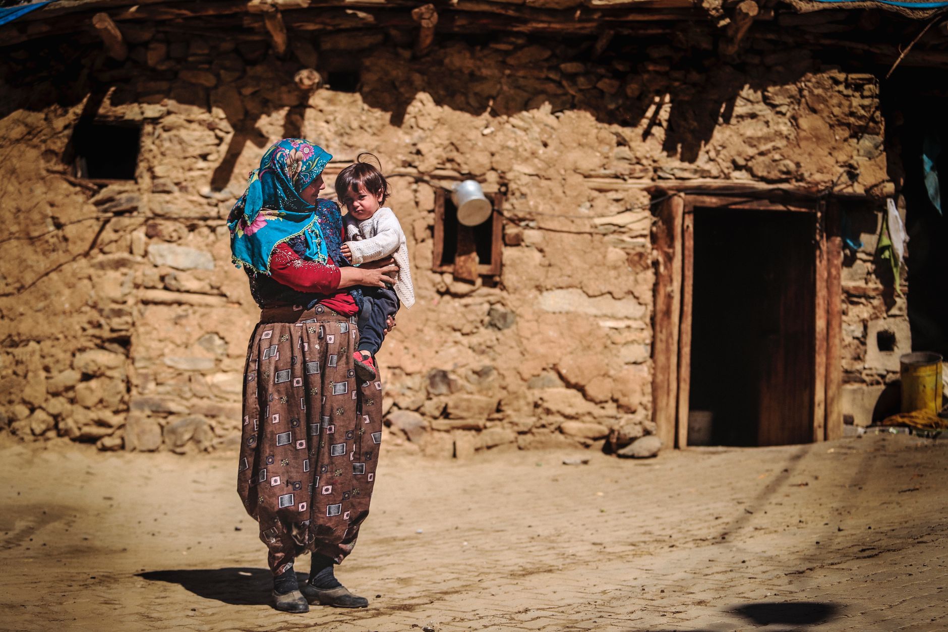 زنی ترک با محبت نوزادی را بیرون خانه‌ای سنگی روستایی در آغوش گرفته است.