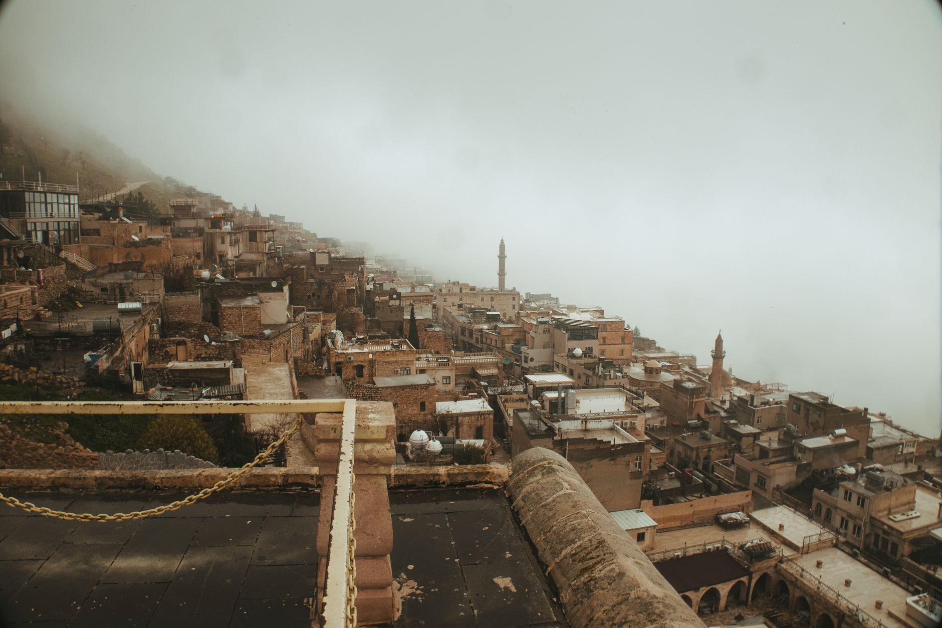 Foggy view of a historic Turkish town with stone buildings and a minaret.