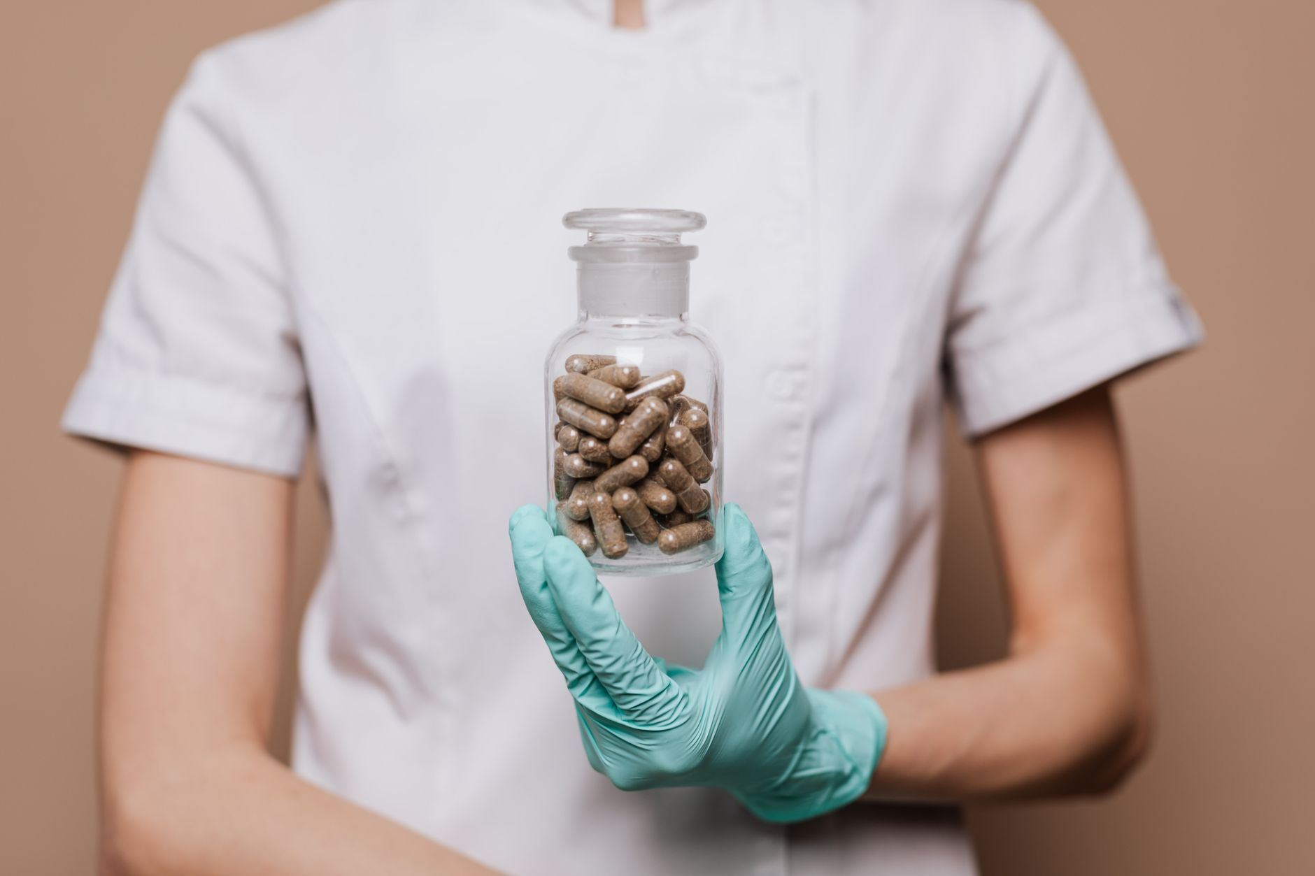 A clinical herbalist in a Turkish hospital holds a glass jar of herbal capsules.
