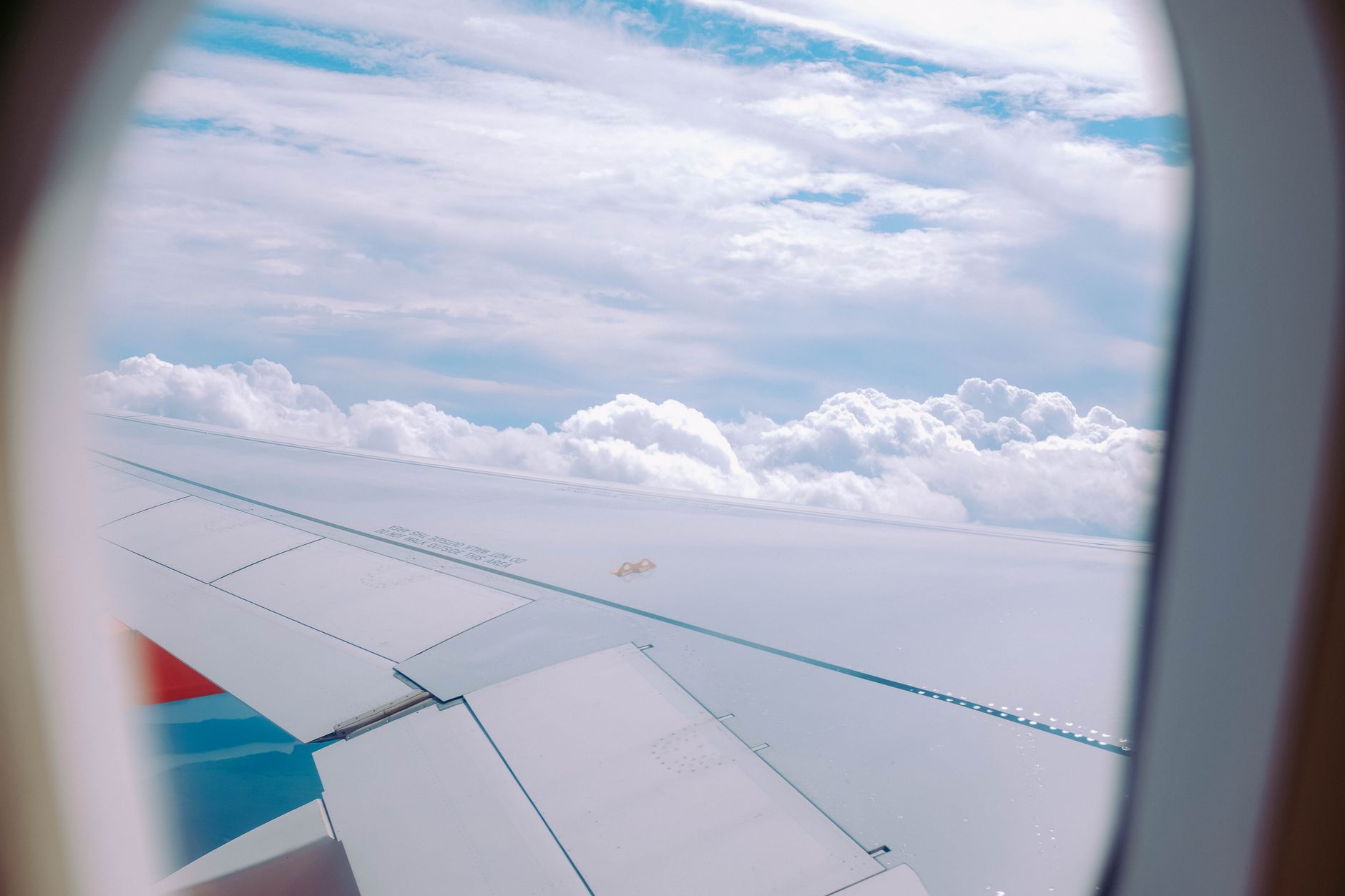 View from an airplane window showing the aircraft wing and fluffy clouds beneath.