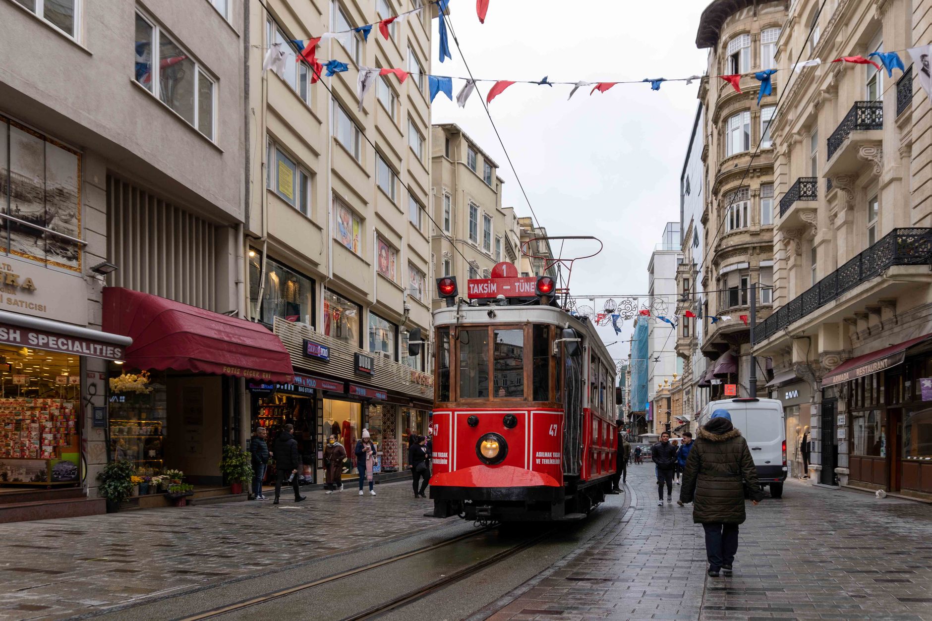 A red tram travels down a lively street in Istanbul amidst shoppers and colorful decorations.