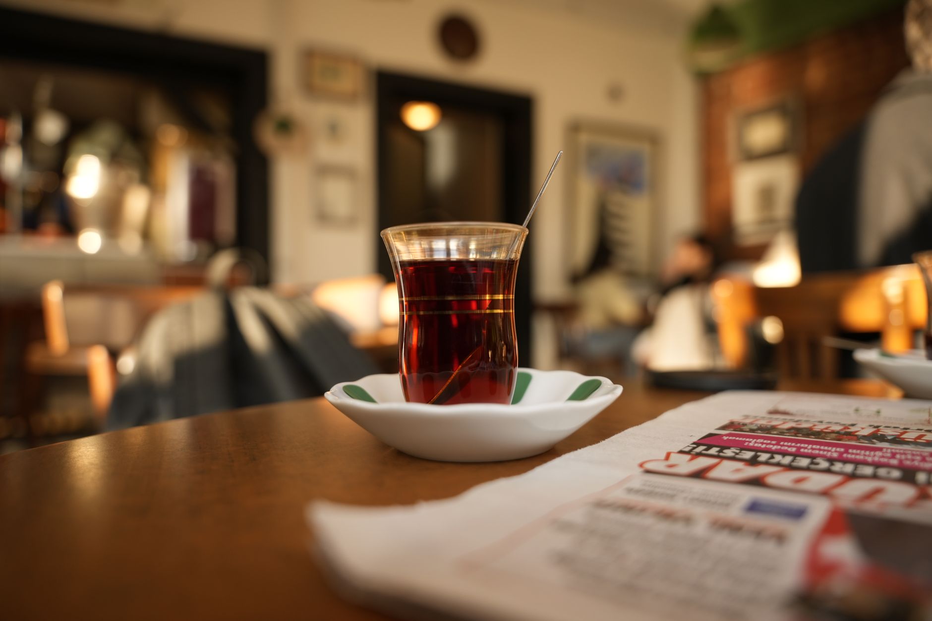 A glass of Turkish tea on a white plate in a warm cafe setting.