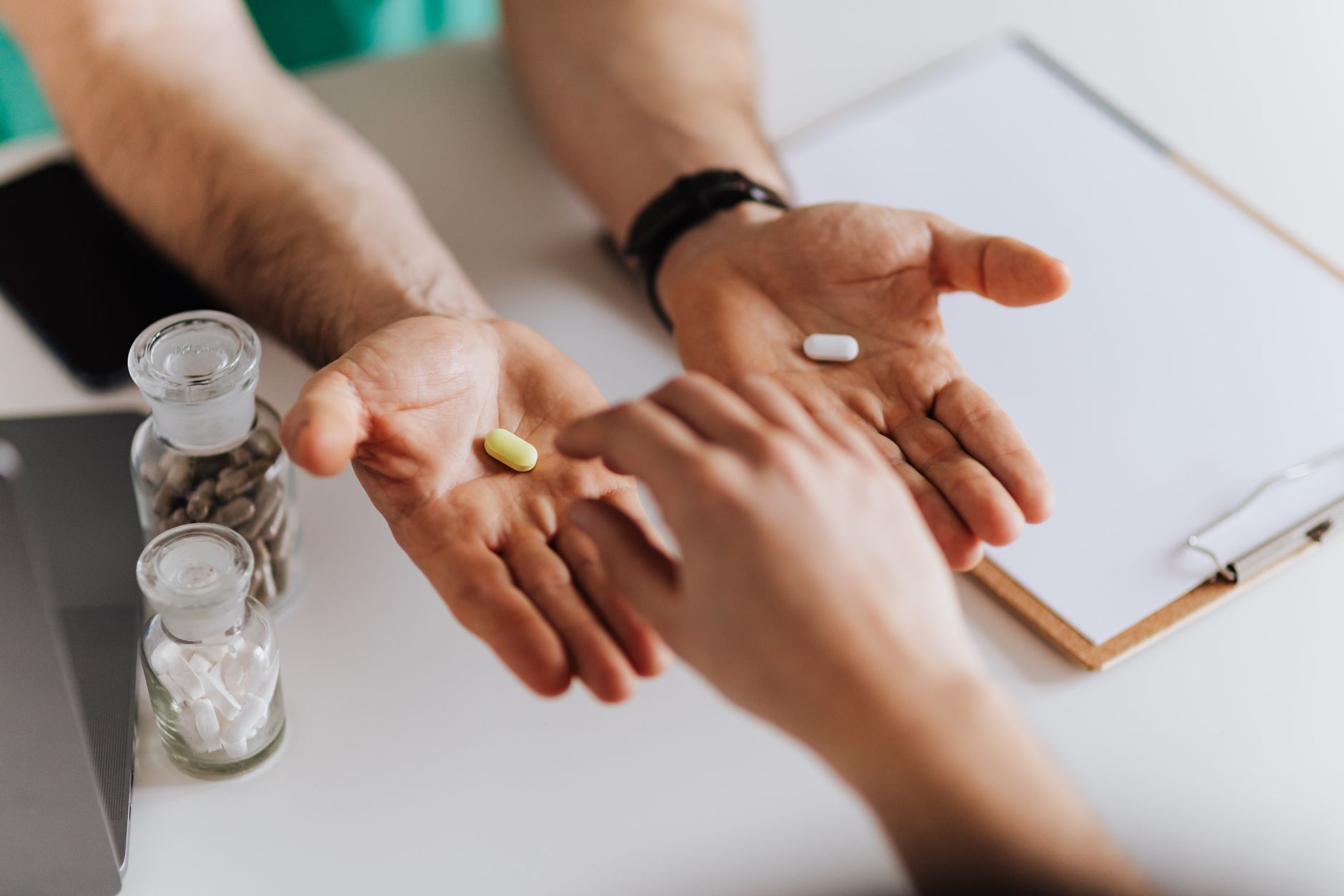 A healthcare professional offers two pills to a patient during a consultation.