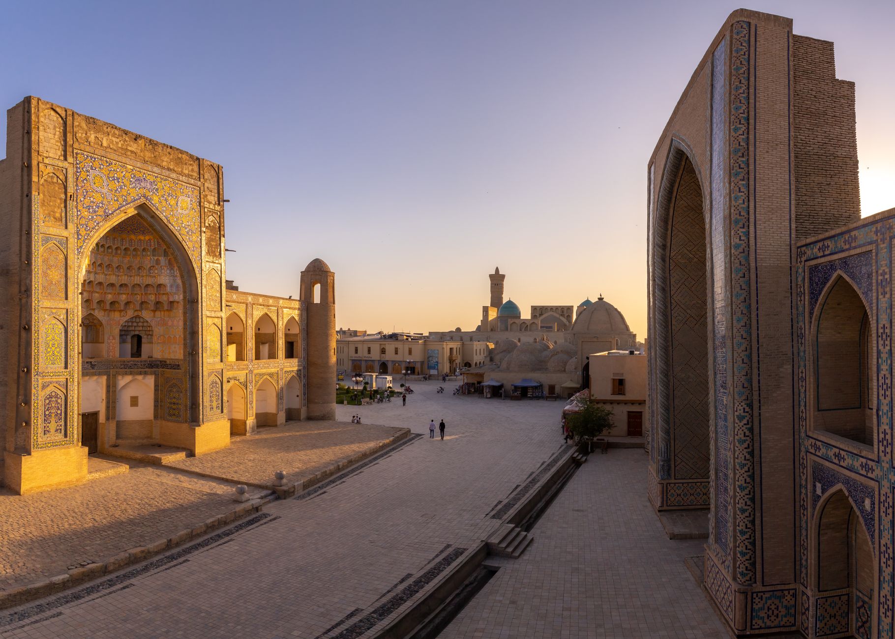 منظر خلاب للعمارة القديمة في بخارى عند غروب الشمس، يتميز ببلاط معقد وساحة مزدحمة.