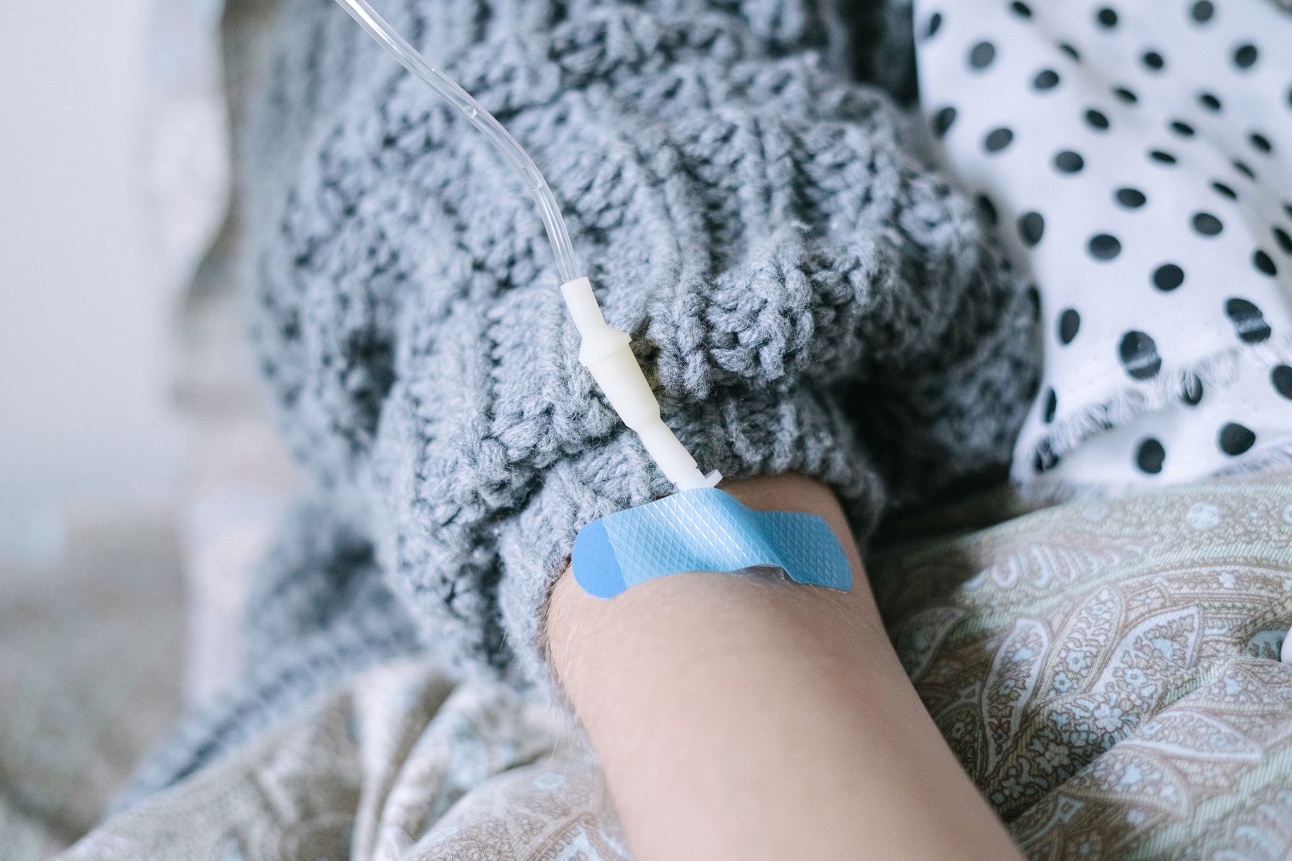 Close-up of a patient's arm with an IV line, wearing a cozy sweater, prepared for chemotherapy in a private setting.