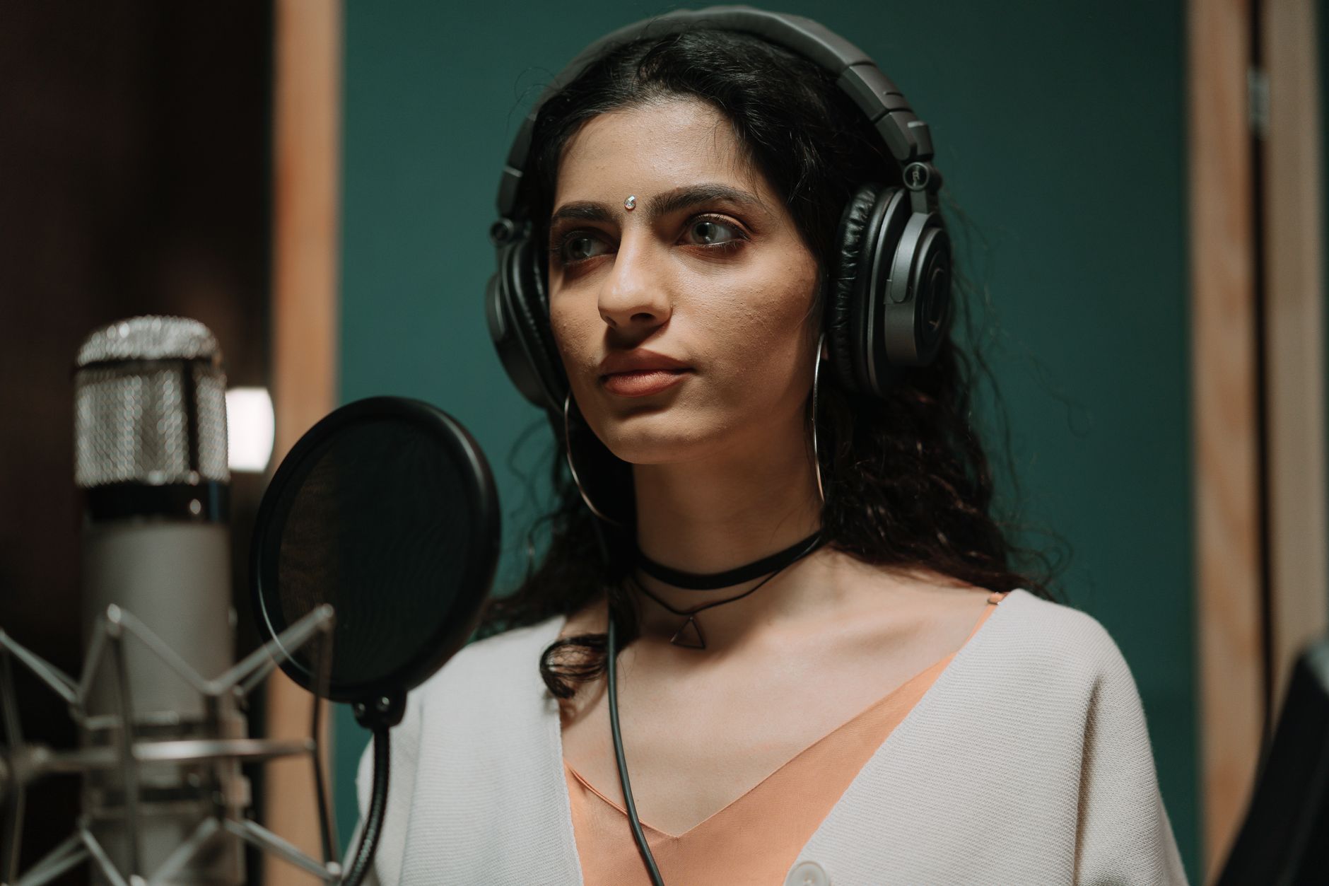 A professional singer wearing headphones stands at a microphone in a recording studio, ready to perform.