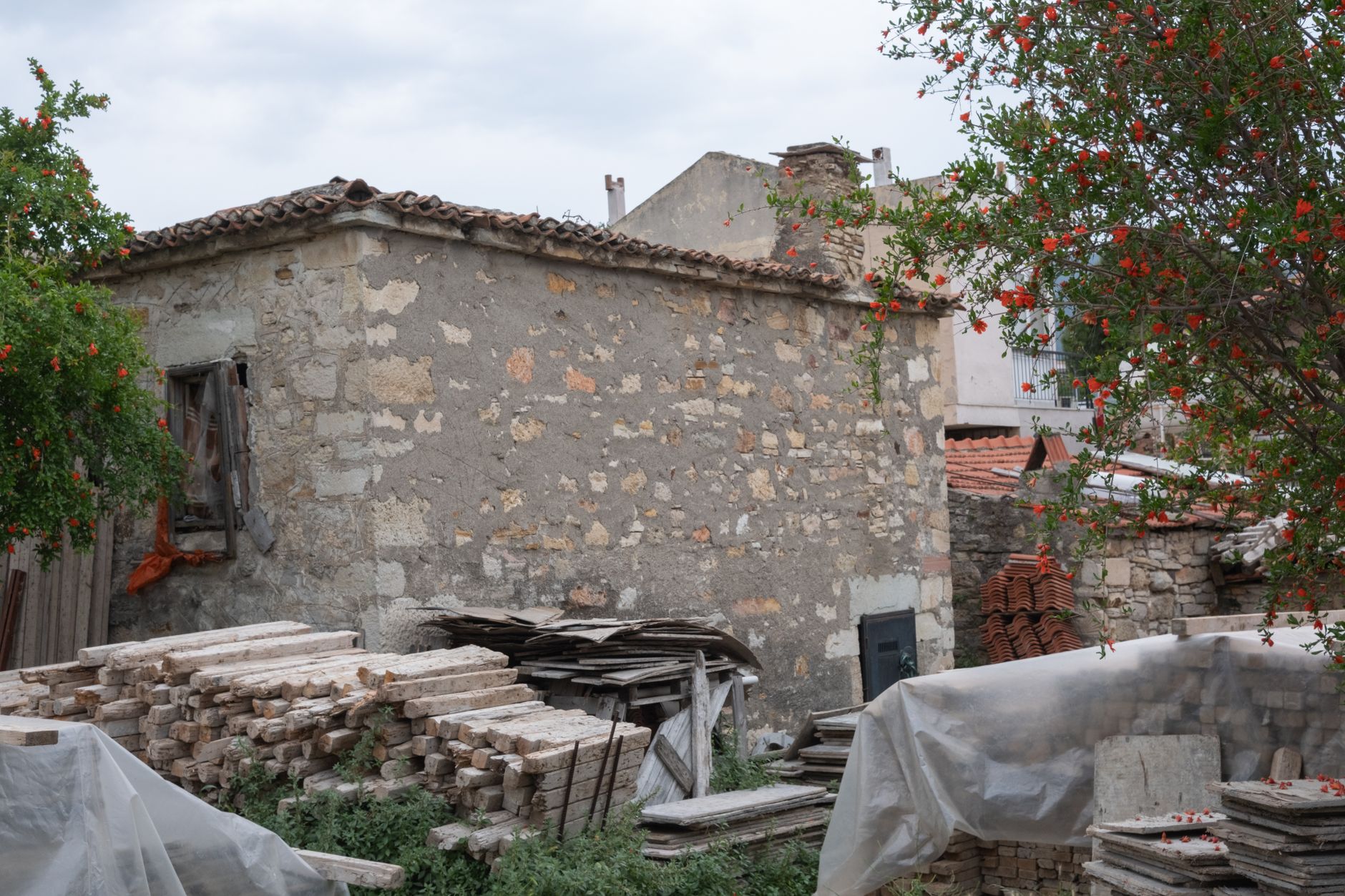 Şirin bir kırsal köyde yapraklarla çevrili, yıpranmış taş bir ev ve üst üste yığılmış ahşap kalaslar.