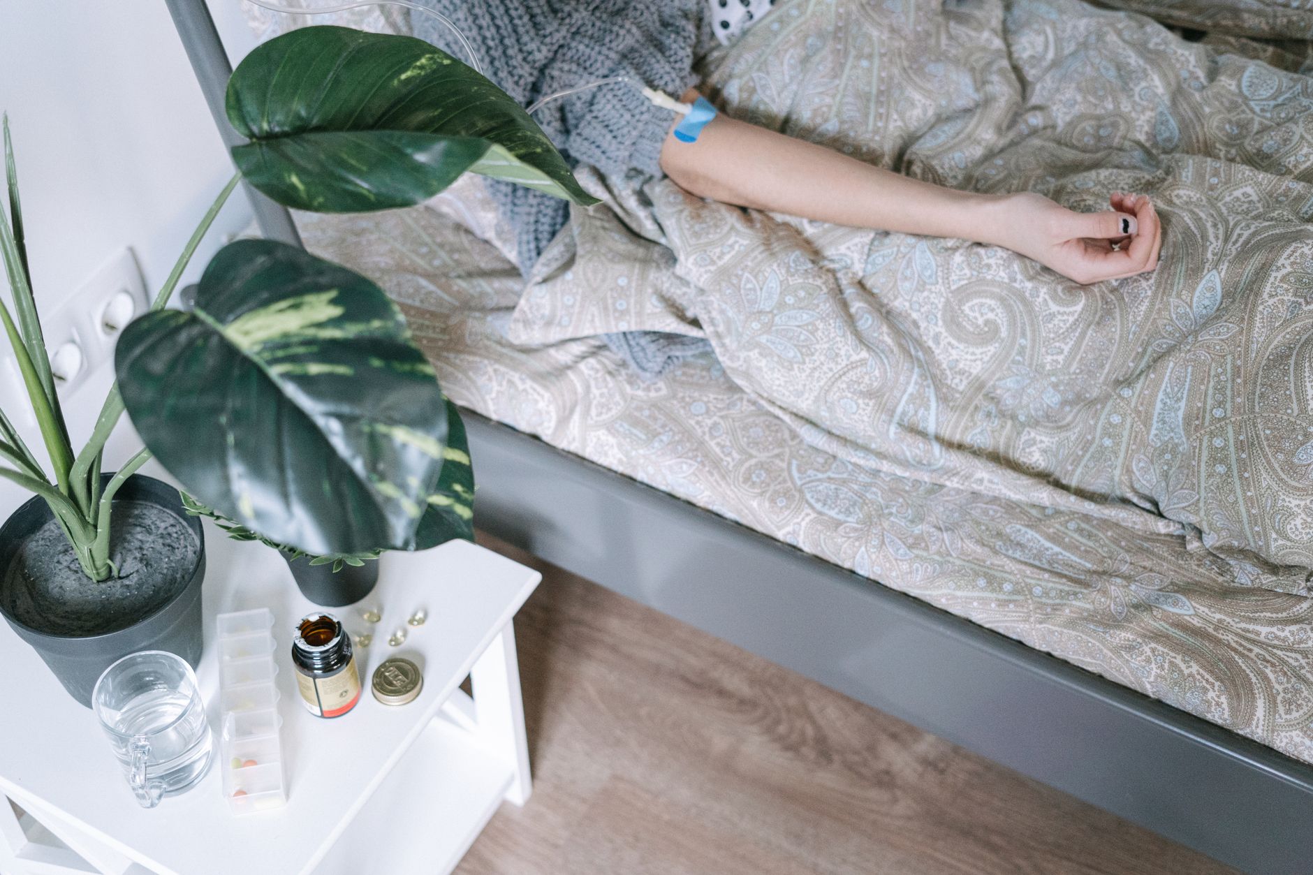 Patient's arm resting outside blankets, with plants and medication nearby.