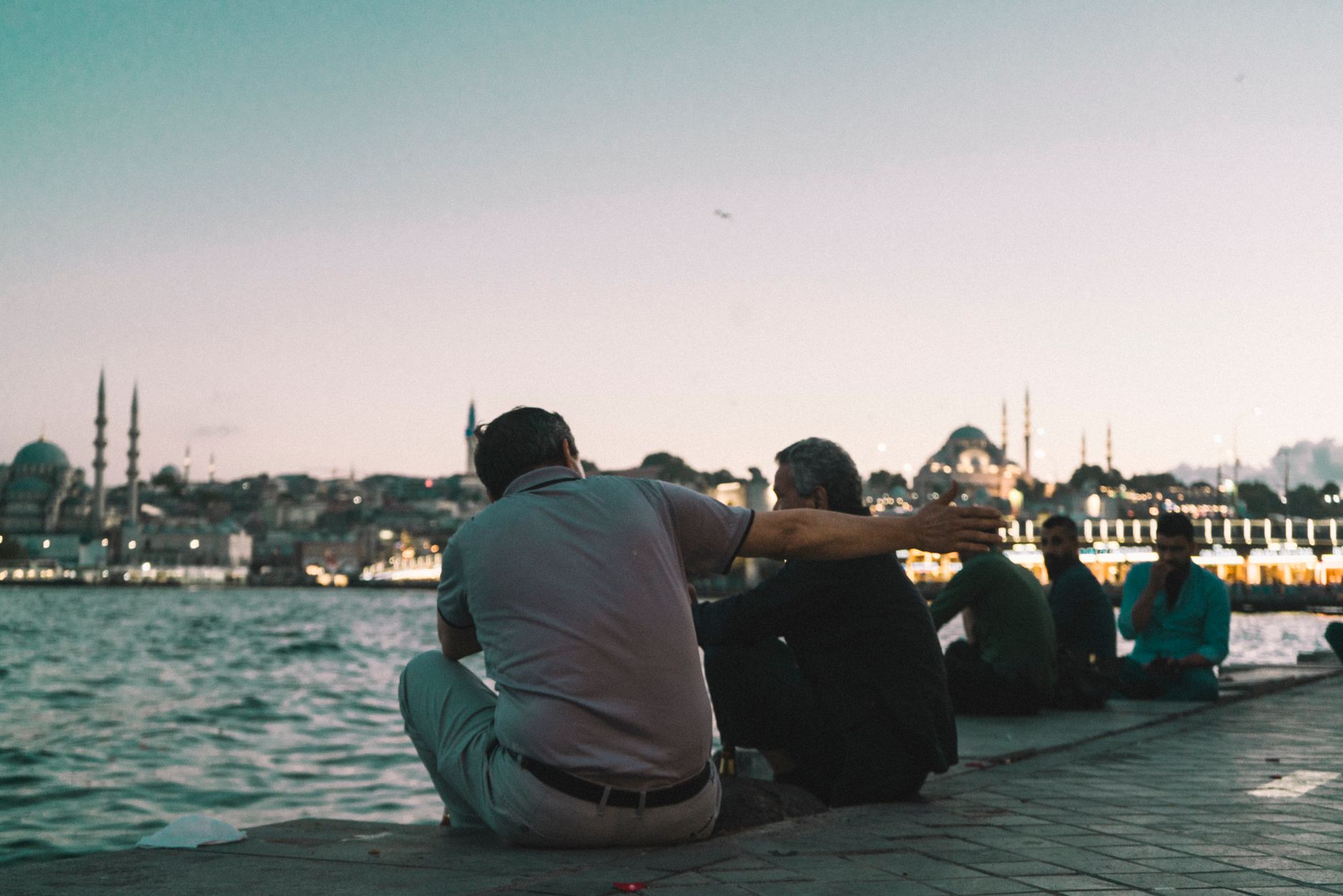 Two friends enjoying a conversation by the Bosphorus in Istanbul at sunset.