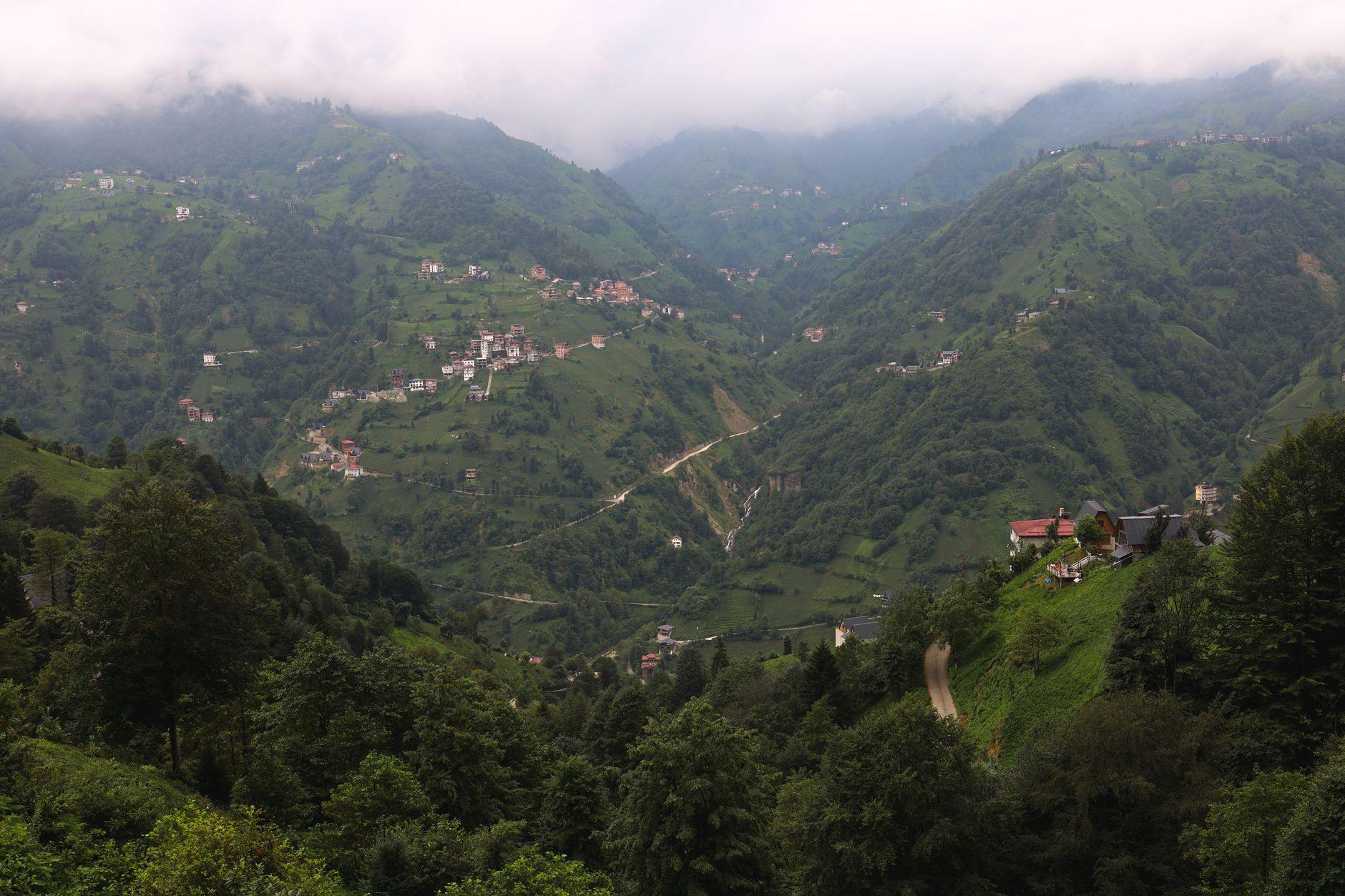 一座风景如画的高原村庄坐落在青山之中，传统石屋与繁花盛开的树木相映成趣。
