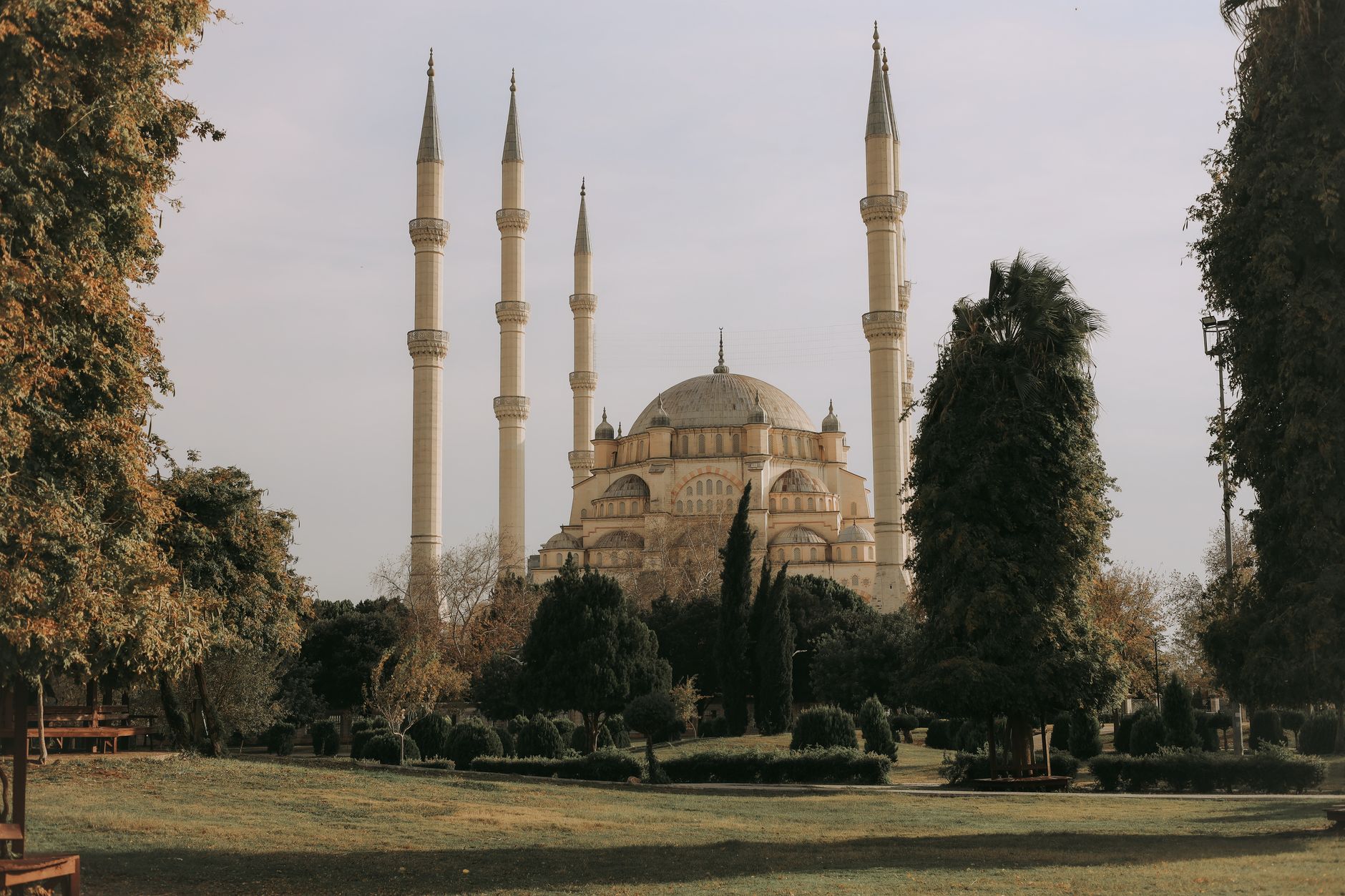View of a grand mosque with multiple minarets nestled among trees and greenery.