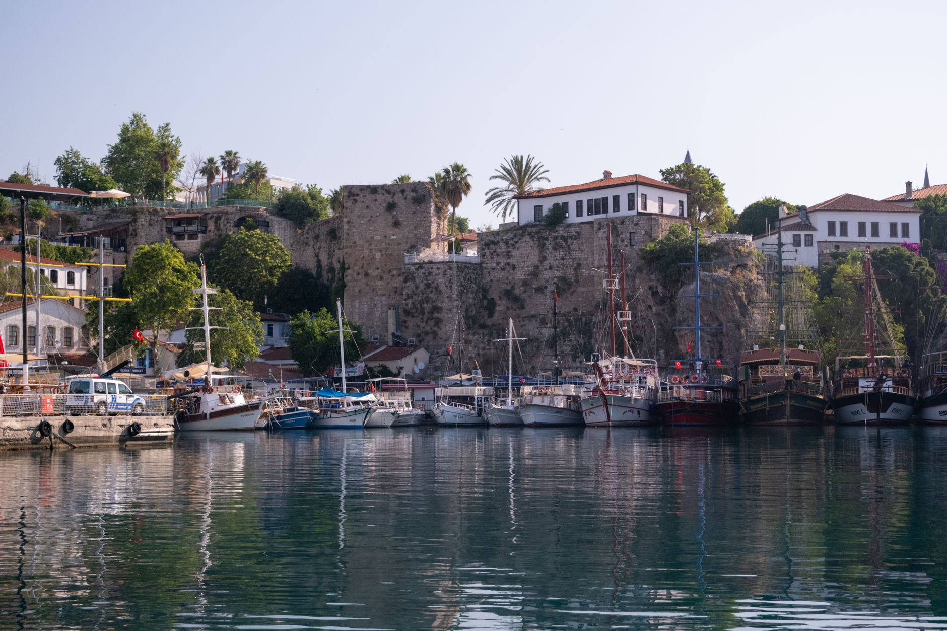 A serene view of Kaleiçi Harbor in Antalya, lined with boats under blue skies.