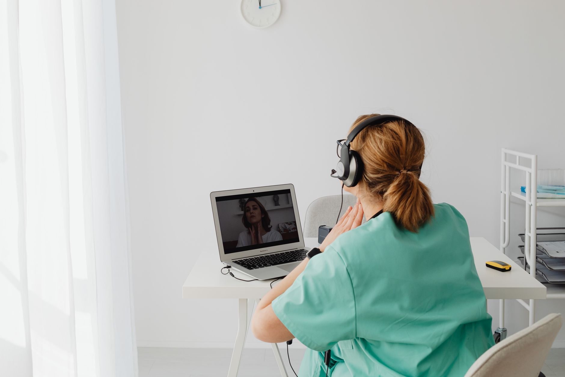 A patient in green scrubs participates in a video consultation with a doctor using a laptop.