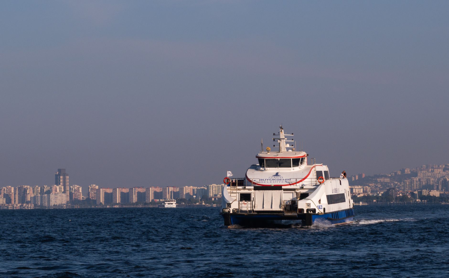 A ferry navigating the waters near Çeşme, with city skyline in the background.