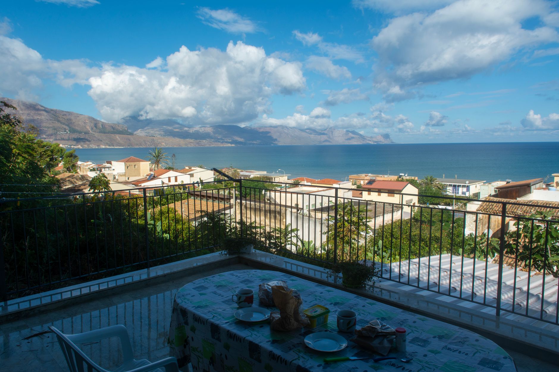 Terrace view of a harbor town with panoramic ocean and mountain backdrop.
