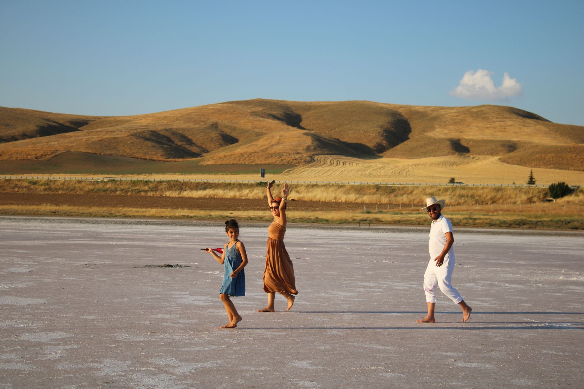 Three people joyfully walking on salt flats with hills in the background.