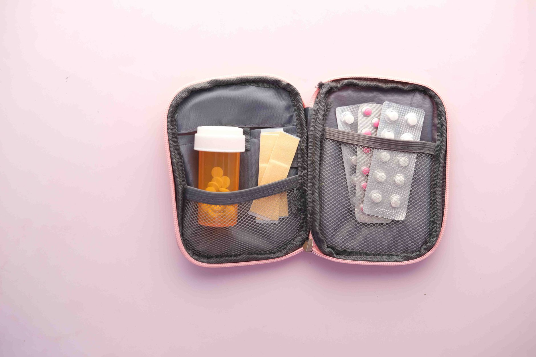 A pink-cased medication organizer featuring prescriptions and pills, ready for travel.