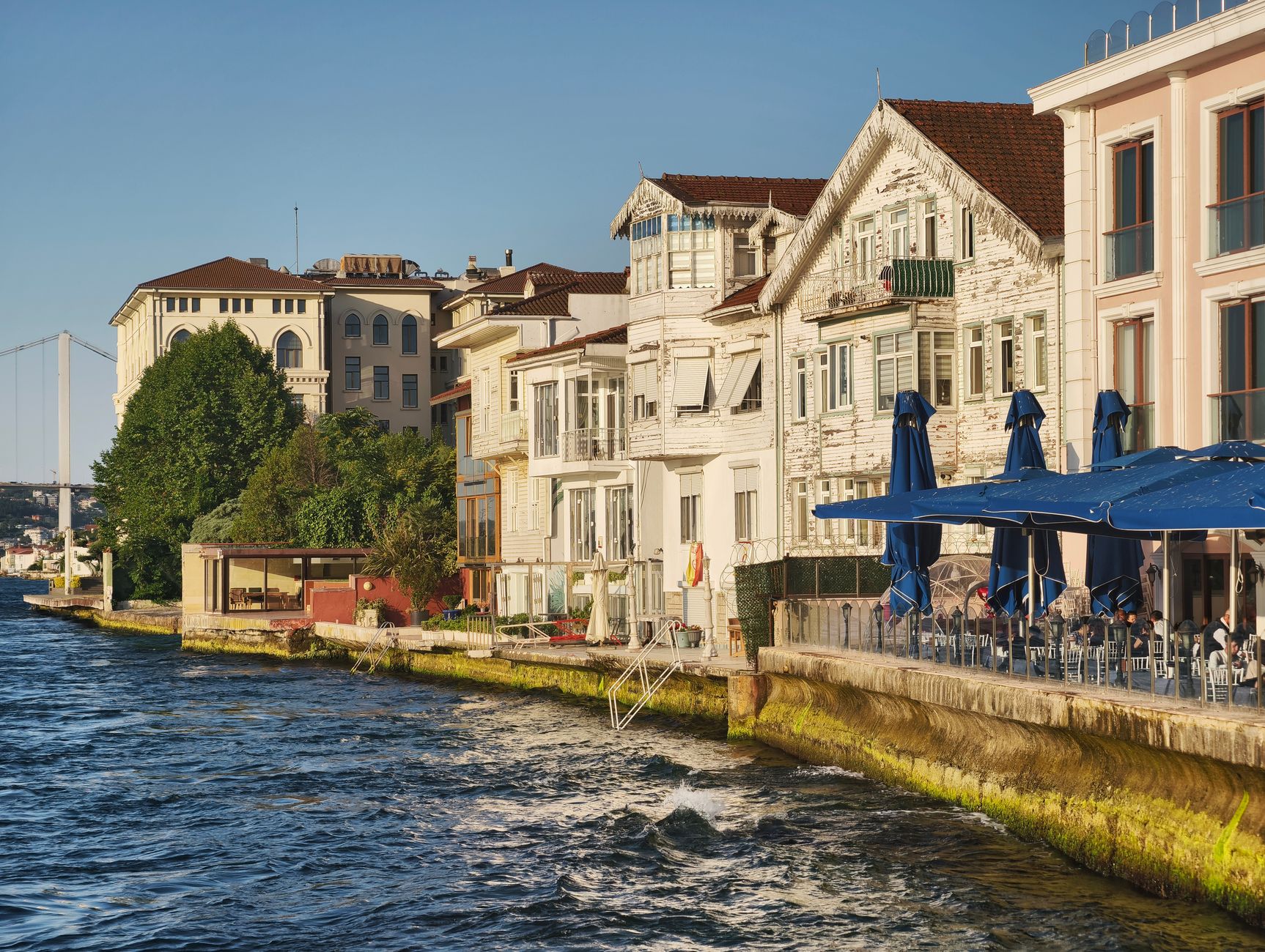 Outdoor café along the Bosphorus with traditional houses and blue umbrellas.