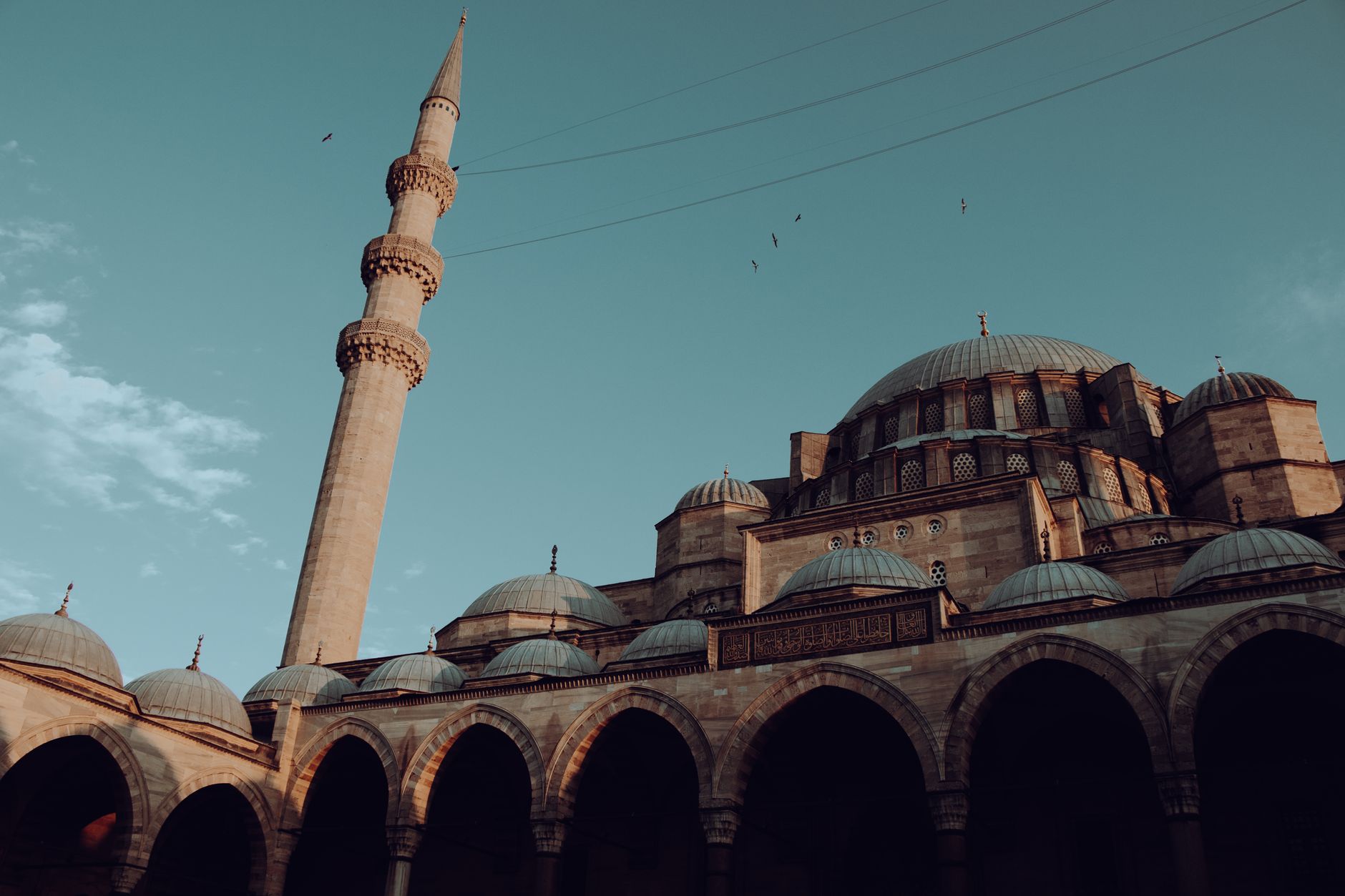 View of a historic mosque in Istanbul featuring ornate domes and a tall minaret against a clear blue sky.
