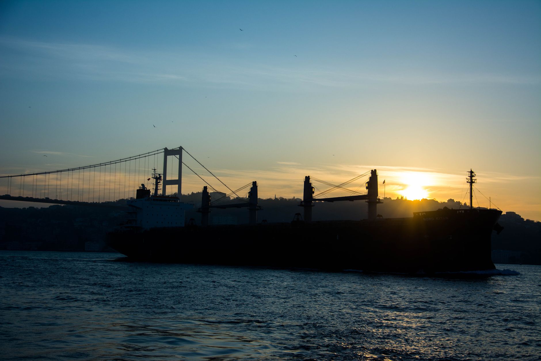Silhouette of a ship on the Bosphorus at sunrise with a bridge in the background.