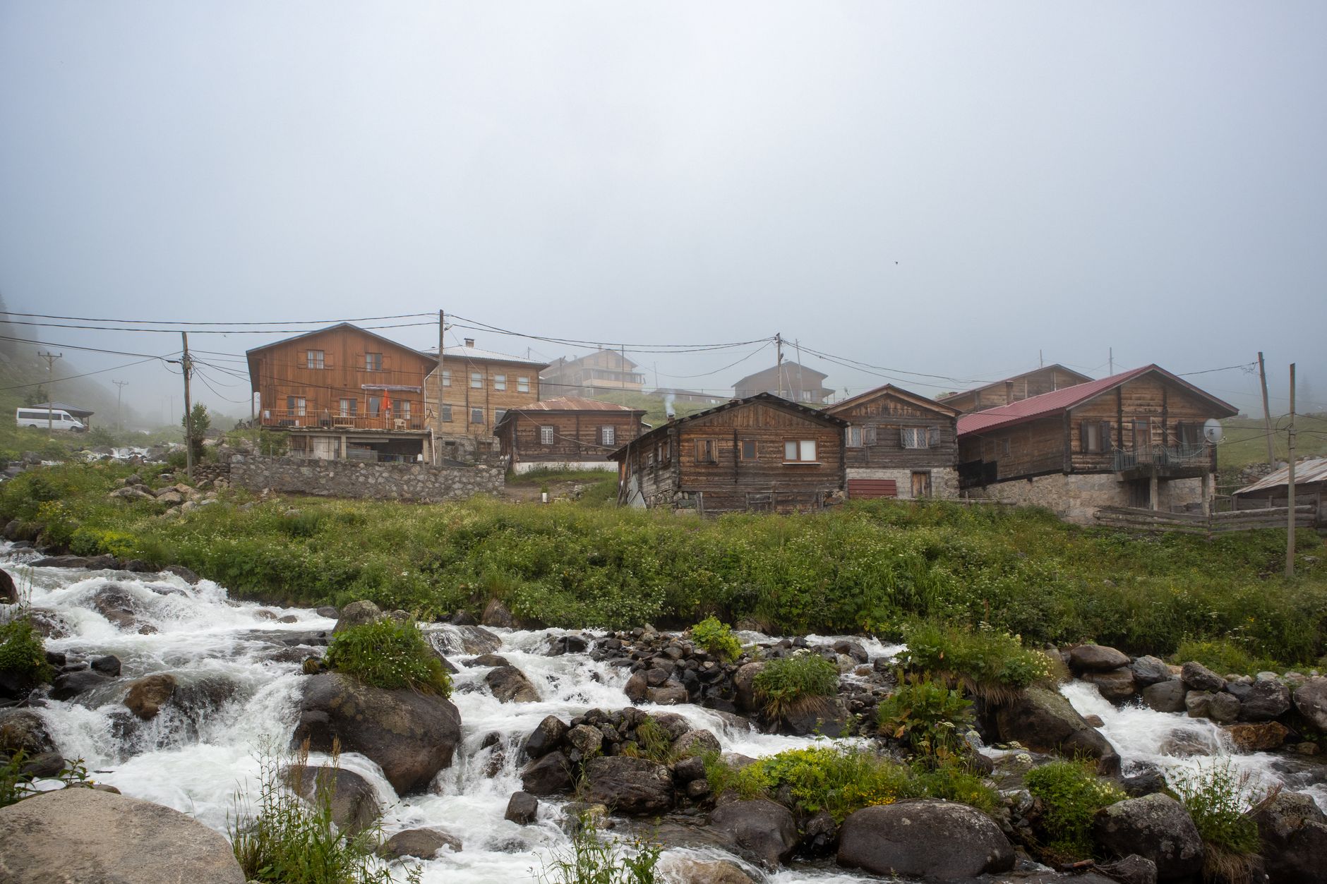 Foggy view of a pastoral village in Çaykara, featuring stone houses and a flowing stream.