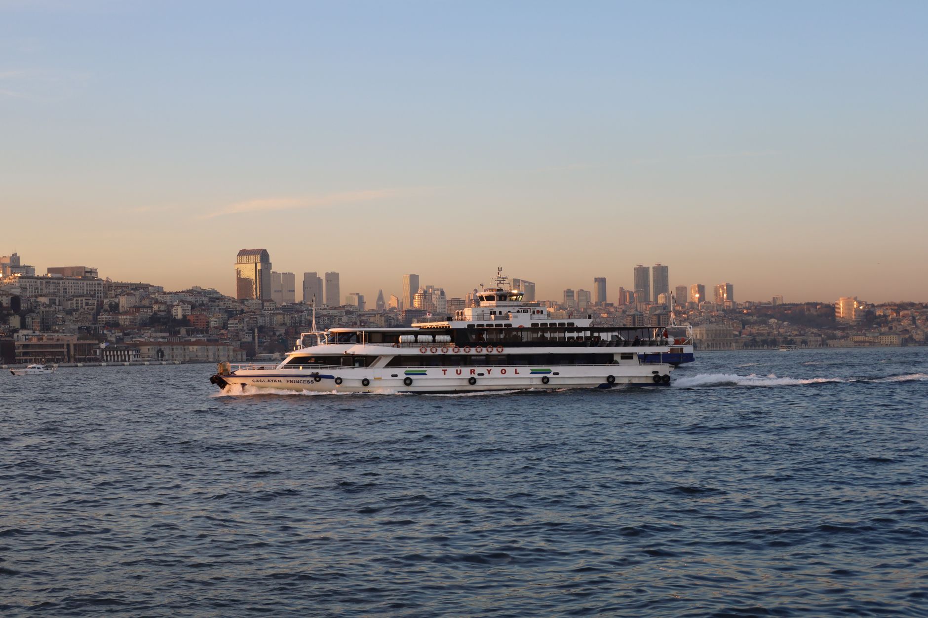 The Calantha Princess boat glides through the Bosphorus, with Istanbul's skyline in the background during sunset.