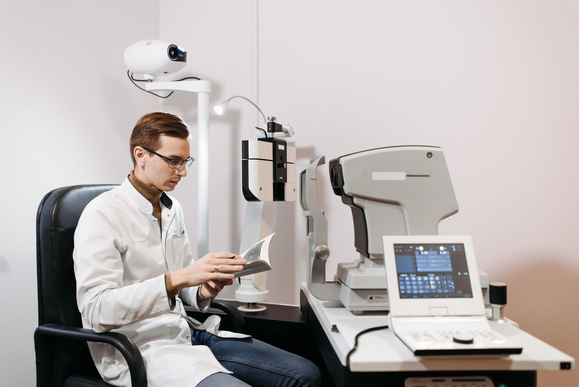 An ophthalmologist reading in a consultation room equipped with eye exam machines.