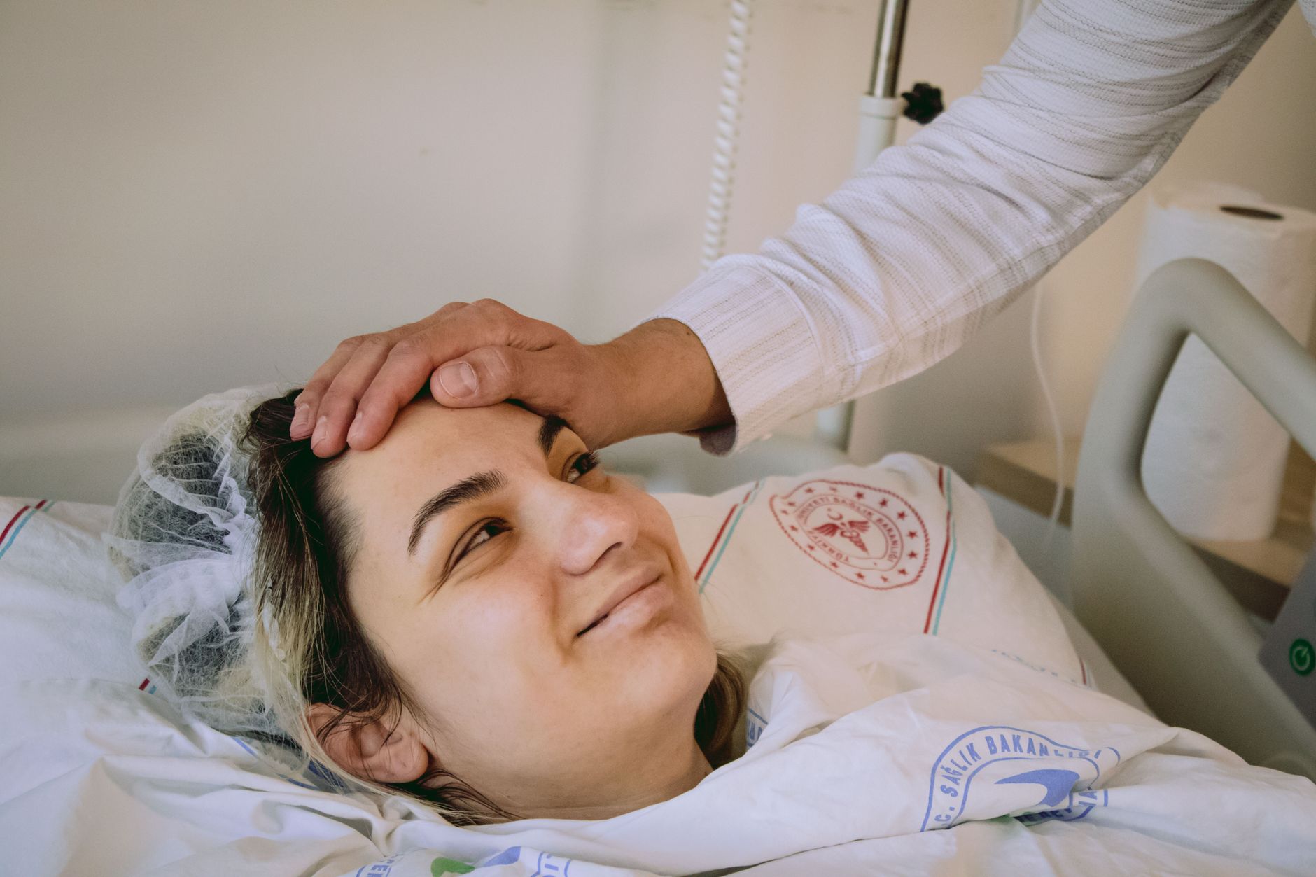 Smiling patient in hospital bed after eye surgery, giving thumbs up.