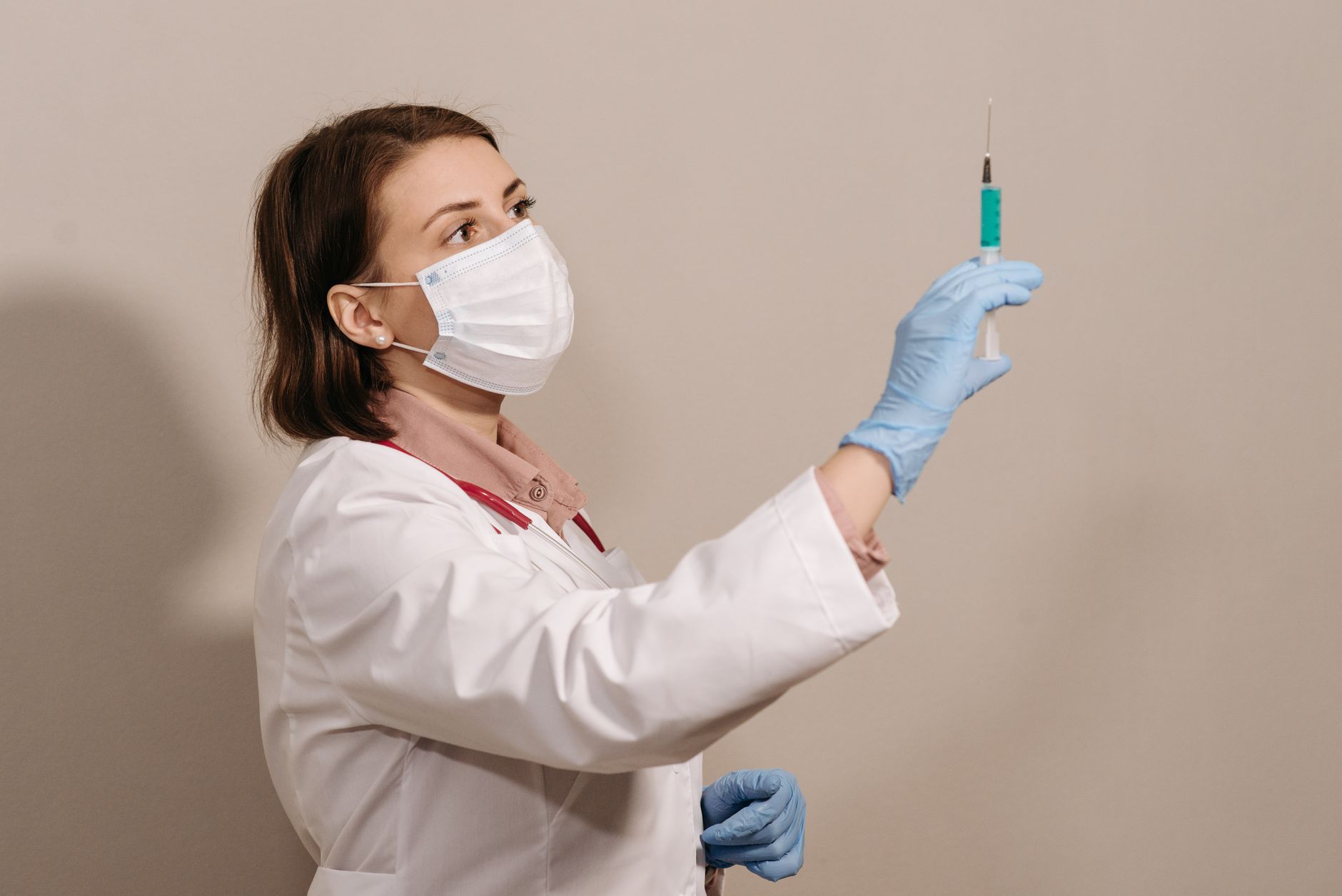 A nurse in a white coat and mask prepares a syringe for a biologic injection.