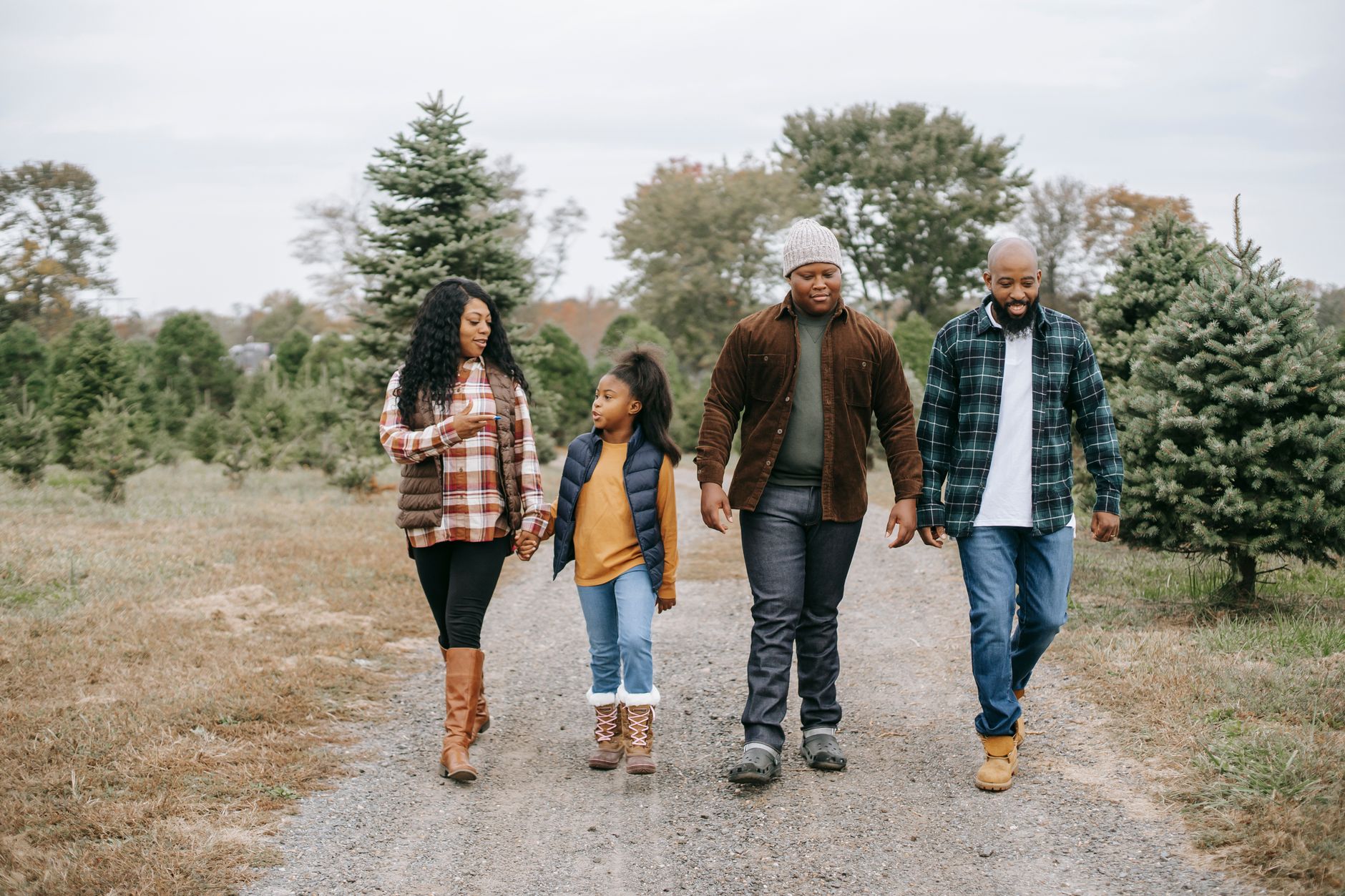 A family of four walking together in a tree farm, enjoying quality time outdoors.