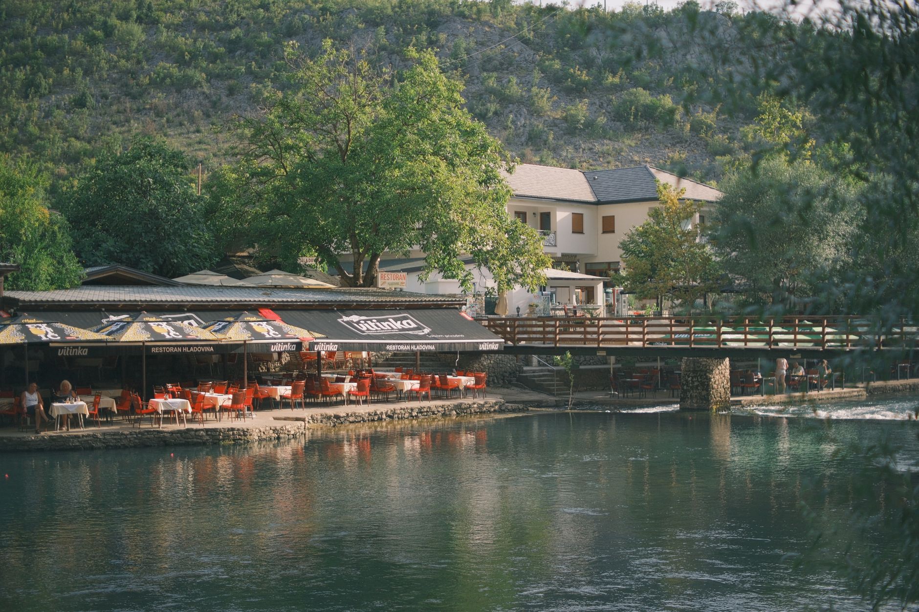 Scenic view of a riverside restaurant with outdoor seating and a rushing stream.
